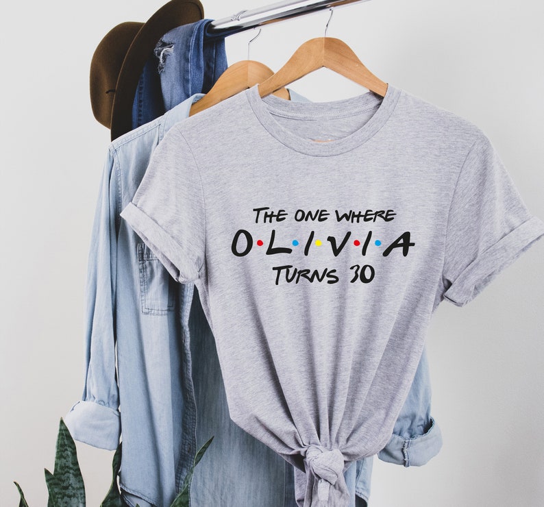 May include: Gray t-shirt with the text "The One Where Olivia Turns 30" in black with colorful dots. The text is styled like the title cards from the TV show Friends.