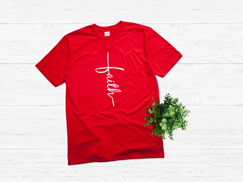 Puede incluir: Camiseta roja con una cruz blanca y la palabra "faith" escrita verticalmente en ella.