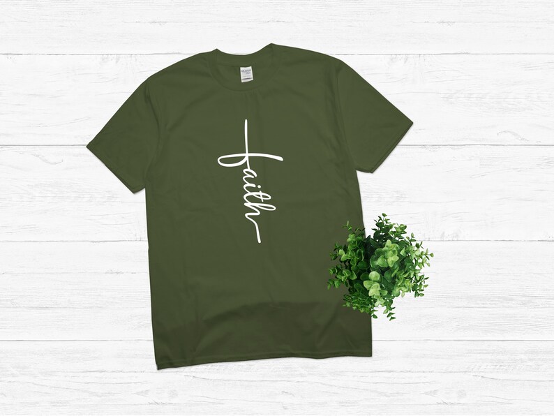 Puede incluir: Una camiseta verde con una cruz blanca y la palabra "faith" escrita verticalmente en ella.