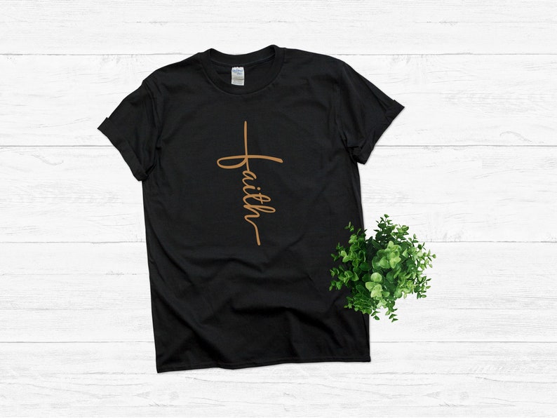 Puede incluir: Camiseta negra con una cruz marr&oacute;n y la palabra "faith" escrita verticalmente en la cruz.