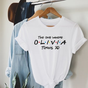 May include: White t-shirt with the text "The One Where Olivia Turns 30" in black with colorful dots. The text is styled like the Friends TV show logo.
