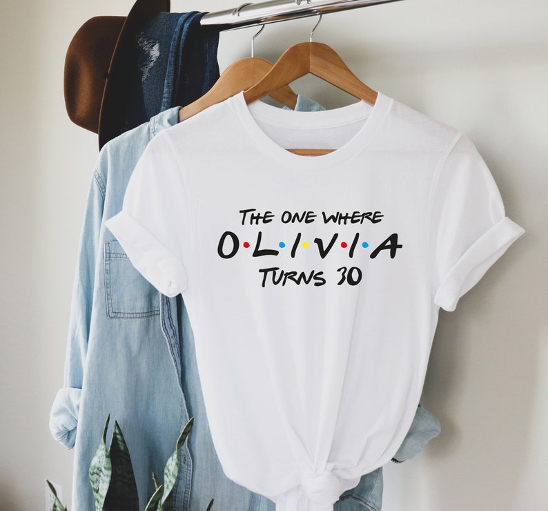 May include: White t-shirt with the text "The One Where Olivia Turns 30" in black with colorful dots. The text is styled like the Friends TV show logo.