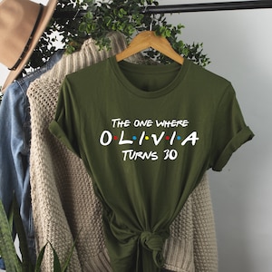 May include: Green t-shirt with the text "The One Where Olivia Turns 30" in white with colorful dots. The shirt is tied in a knot at the bottom.