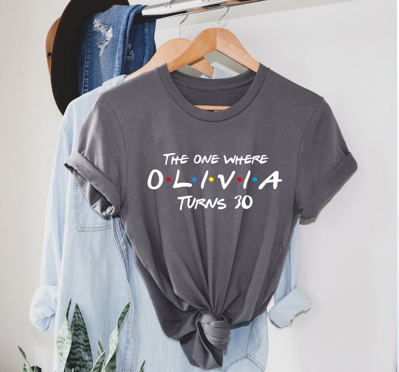 May include: Gray t-shirt with the text "The One Where Olivia Turns 30" in a white font. The text is styled to look like the title card from the TV show Friends.