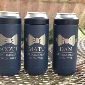 May include: Three blue Yeti Rambler 12 oz.  cans with a silver bow tie design and personalized text. The text reads "Scott Groomsman 04.24.2021", "Matt Groomsman 04.24.2021", and "Dan Groomsman 04.24.2021".