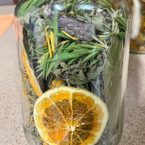Puede incluir: Un tarro de vidrio lleno de hierbas secas, flores y una rodaja de naranja seca. El tarro tiene un cordel alrededor de la tapa.