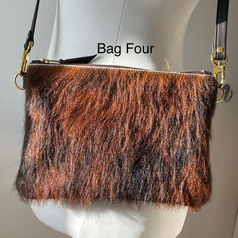 May include: A rectangular crossbody bag with a brown and black fur-like texture. The bag has a zipper closure and gold-colored hardware. The text "Bag Four" is printed on the top of the bag. The bag has a black strap.