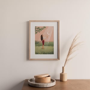 Puede incluir: Una impresi&oacute;n art&iacute;stica enmarcada representa a una persona de pie en un campo, con los brazos extendidos hacia una luna creciente. La obra de arte presenta una paleta de colores rosa, verde y blanco, con una rama de &aacute;rbol en la esquina superior izquierda.