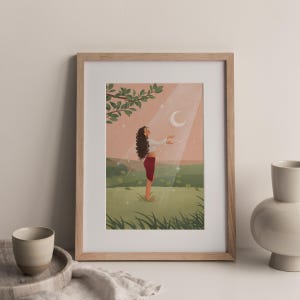 Puede incluir: Una impresi&oacute;n art&iacute;stica enmarcada representa a una persona de pie en un campo, con los brazos extendidos hacia una luna creciente y rayos de luz. La persona lleva una parte superior blanca y pantalones rojos. El fondo presenta un cielo rosa, colinas verdes y una rama de &aacute;rbol.