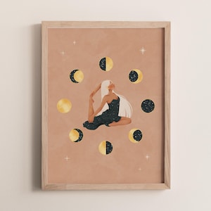 May include: A framed art print featuring a woman in a yoga pose surrounded by phases of the moon. The artwork has a warm, neutral background with gold and navy blue accents. The woman has long white hair and is wearing a dark dress.
