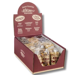 May include: A display box of Amish Country popcorn in a burgundy-colored cardboard box. The box features various popcorn varieties, including Blue, Ladyfinger, and Red. Each bag pops four quarts. The box is labeled "Amish Country Popcorn."