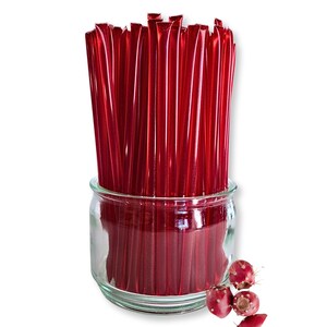 May include: A clear glass jar filled with numerous red honey sticks. Several red prickly pears are scattered near the jar. The honey sticks are individually wrapped and appear to be filled with a red liquid.