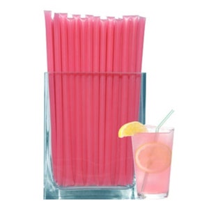 May include: A glass vase filled with pink, single-use, plastic straws. The straws are in a clear glass vase with a square base. A glass of pink lemonade with a lemon wedge and a green straw is in the foreground.