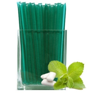 May include: A clear glass square container filled with green straws. Beside the container are three white pieces of chewing gum and a sprig of fresh mint with green leaves.