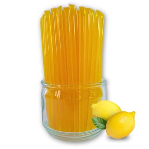 May include: A clear glass jar filled with numerous yellow honey sticks. Two yellow lemons and a green leaf are next to the jar. The honey sticks are a bright yellow color.