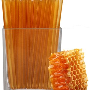 May include: A clear glass container filled with individual honey sticks, alongside a piece of honeycomb. The honey sticks are a translucent amber color, and the honeycomb is a rich, golden hue. The image is set against a white background.