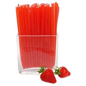 May include: A clear glass jar filled with red honey sticks, with two fresh red strawberries in the foreground.