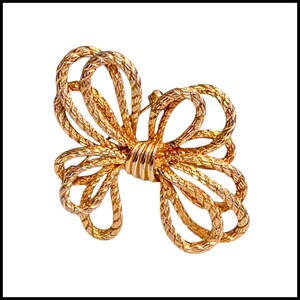 May include: A gold-toned bow brooch with a textured, woven design. The brooch is shaped like a bow with multiple loops and a central knot. The pin is a classic accessory, suitable for adding a touch of elegance to any outfit.