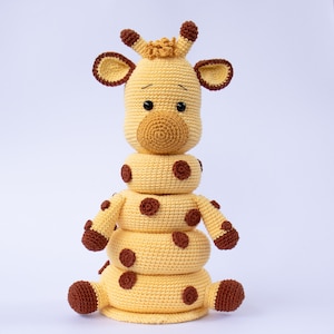 May include: A crocheted giraffe toy with brown spots and a stack of yellow rings. The giraffe has a brown nose and black eyes.