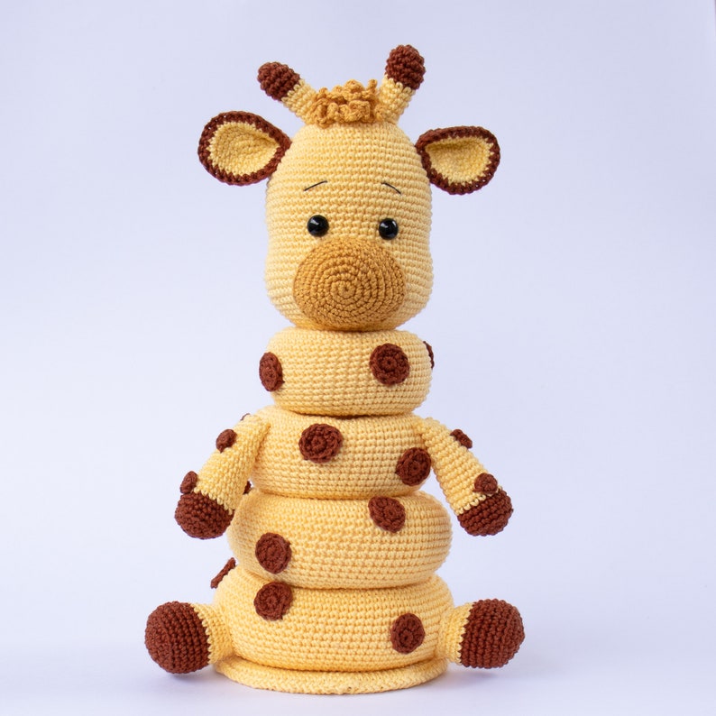 May include: A crocheted giraffe toy with brown spots and a stack of yellow rings. The giraffe has a brown nose and black eyes.