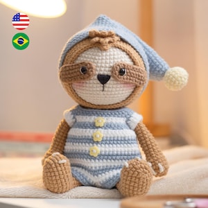 Puede incluir: Una muñeca de perezoso de ganchillo hecha a mano que lleva un pelele a rayas azules y blancas y un gorro de dormir a juego con un pompón amarillo. El perezoso tiene detalles marrones alrededor de los ojos y en los brazos y las piernas.