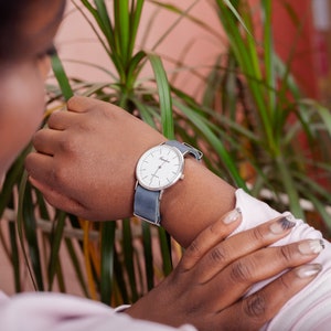 May include: A person wearing a white watch with a silver face and a blue canvas band.