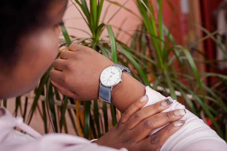May include: A person wearing a white watch with a silver face and a blue canvas band.