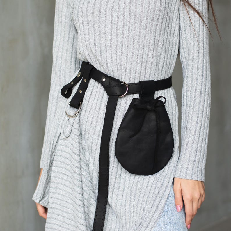 May include: A black leather belt with a small black pouch attached. The belt has silver hardware and is worn over a gray sweater.