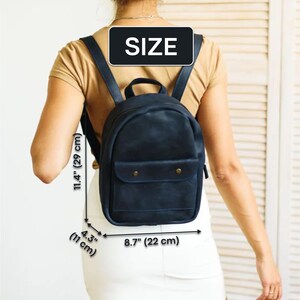 May include: A dark blue leather backpack with a flap pocket and a zipper closure. The backpack measures 11.4 inches tall, 8.7 inches wide, and 4.3 inches deep.
