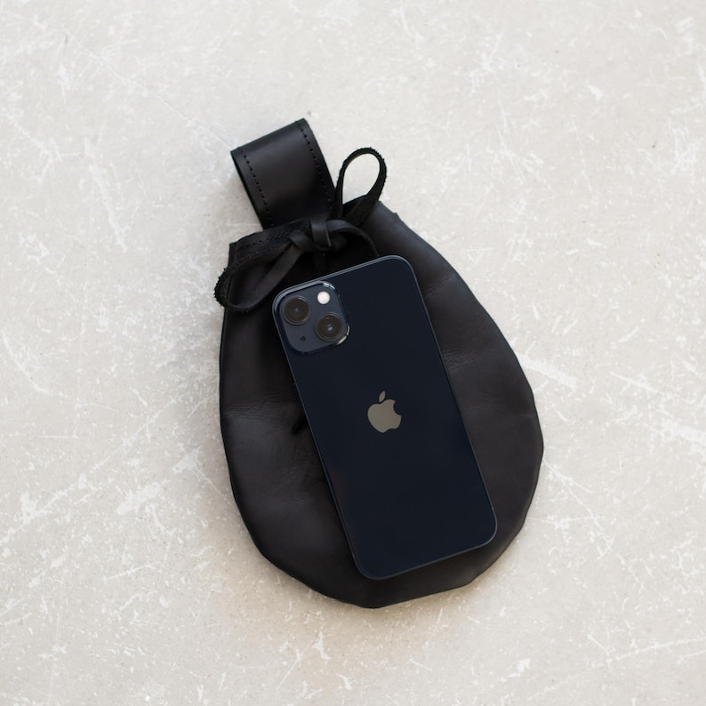 May include: A black leather pouch with a drawstring closure, holding a dark blue iPhone with a black camera lens and an Apple logo.