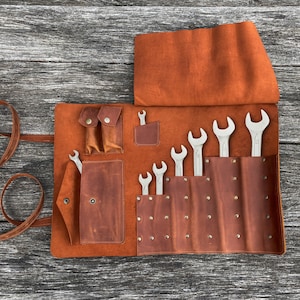 May include: A brown leather tool roll with multiple pockets and a flap closure. The roll is open and contains a set of wrenches.