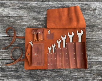 May include: A brown leather tool roll with multiple pockets and a flap closure. The roll is open and contains a set of wrenches.
