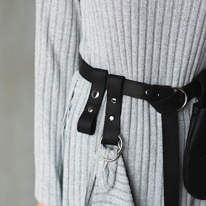 May include: A gray ribbed sweater with a black leather belt with silver hardware. The belt has two straps with buckles and a ring.