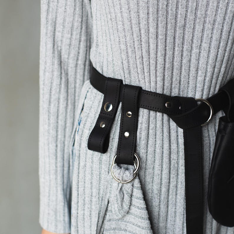 May include: A gray ribbed sweater with a black leather belt with silver hardware. The belt has two straps with buckles and a ring.
