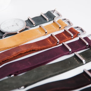 May include: A set of six leather watch straps in various colors, including dark green, mustard yellow, brown, burgundy, olive green, and black. Each strap has silver metal buckle closures.