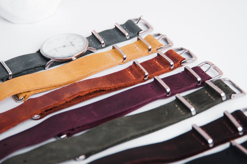 May include: A set of six leather watch straps in various colors, including dark green, mustard yellow, brown, burgundy, olive green, and black. Each strap has silver metal buckle closures.