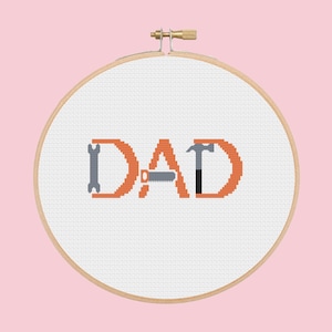 May include: A white embroidery hoop with the word "DAD" in orange letters. The letters are made up of tools like a hammer, saw, and wrench.