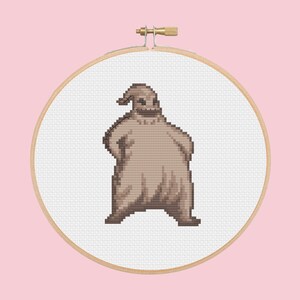 May include: A brown and white cross-stitch embroidery of a character from the movie The Nightmare Before Christmas. The character is a tall, thin, and lanky figure with a large head and a wide smile. The character is wearing a brown sackcloth-like outfit and has a pointed hat.