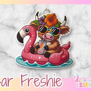 May include: A colorful car freshener featuring a cartoon Highland cow wearing sunglasses and a flower crown, riding a pink flamingo float in a blue pool. The text "Car Freshie" is printed below the image.