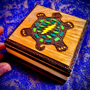May include: A wooden box with a carved turtle design. The turtle is painted with green, yellow, and brown colors. The box is made of light and dark wood.