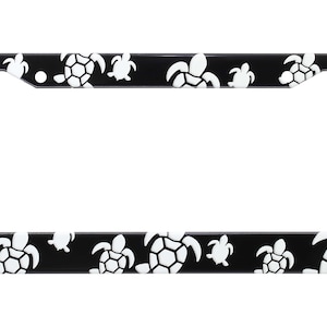 May include: Black license plate frame with a white sea turtle design.
