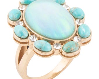 May include: A gold-toned ring featuring a large, oval, opalescent center stone surrounded by smaller turquoise-colored stones and clear crystals. The ring has a detailed, ornate design, showcasing a blend of colors and textures.