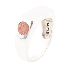 May include: A silver ring with a rectangular top and a circular, reddish-brown stone inlay. The ring has a smooth, polished finish and the word "BARSE" is engraved on the inside.