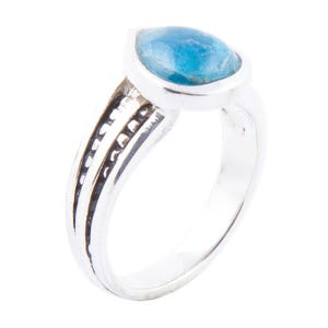 May include: A silver ring featuring a pear-shaped, light blue gemstone. The band has a split design with decorative black accents. The gemstone is set in a silver bezel, creating a striking contrast.