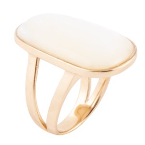 May include: A gold ring with a large, rectangular white stone set in the center. The ring has a double band design.
