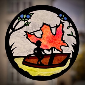 May include: A circular stained glass art piece featuring a silhouette of a person in a boat, with a large red and orange maple leaf. The design includes branches with blueberries and green leaves, set against a cloudy background.