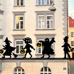 May include: Silhouettes of five figures dressed in Halloween costumes, including a witch, a ghost, and a goblin, holding jack-o'-lanterns. The figures are positioned in front of a building with windows.