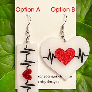 May include: Two pairs of earrings with a white heart shape and a black heartbeat line. One pair has a red glitter heart on the heartbeat line. The other pair has a red glitter heart below the heartbeat line. The earrings are labeled "Option A" and "Option B".