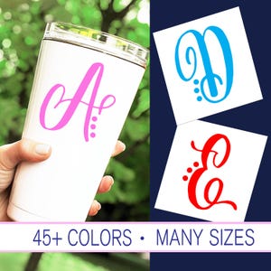 May include: A white tumbler with a pink cursive letter A with three pink dots on the side.  The tumbler is being held by a hand.  Two separate white squares are shown with a blue cursive letter D with three blue dots and a red cursive letter E with three red dots.