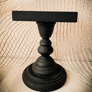 May include: A black wooden pedestal with a rectangular top. The pedestal is made of turned wood and has a smooth, polished finish.